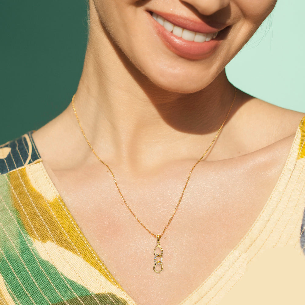 Woman wearing a gold necklace with cubic zirconia pave on a green and blue background