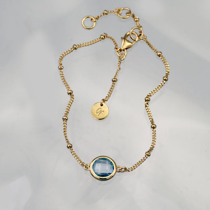 Gold vermeil beaded chain bracelet with blue topaz on a reflective background