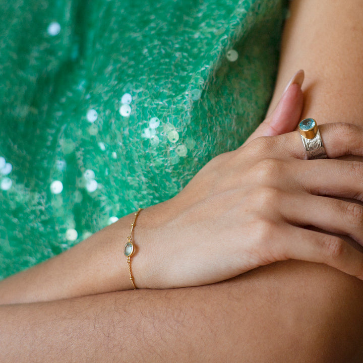 Woman wearing a gold vermeil beaded chain bracelet with blue topaz