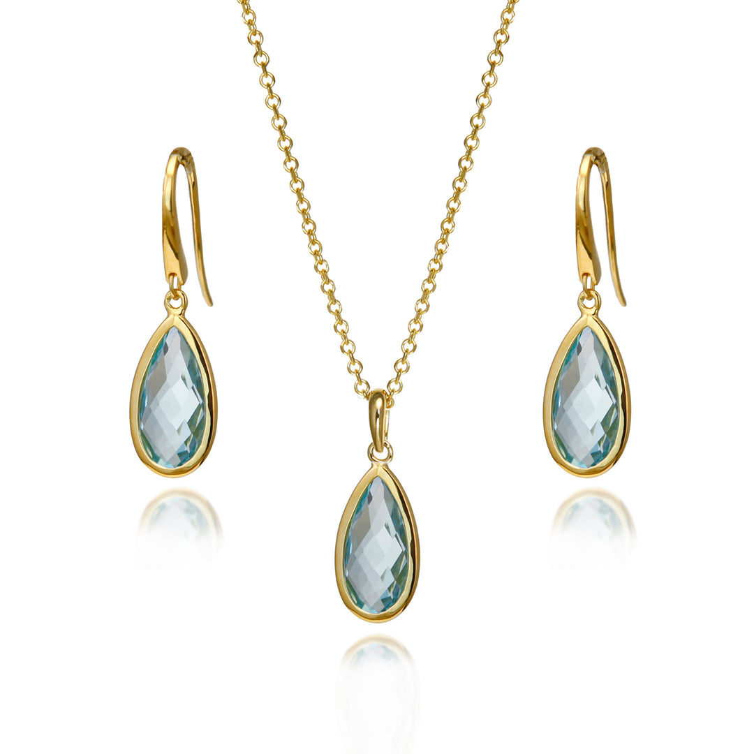 Gold jewelry set featuring a necklace and matching drop earrings with faceted light blue teardrop gemstones, displayed on a clean white background with subtle reflections.