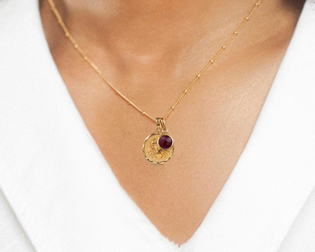 Close-up of woman wearing a gold vermeil zodiac pendant with a ruby birthstone charm.