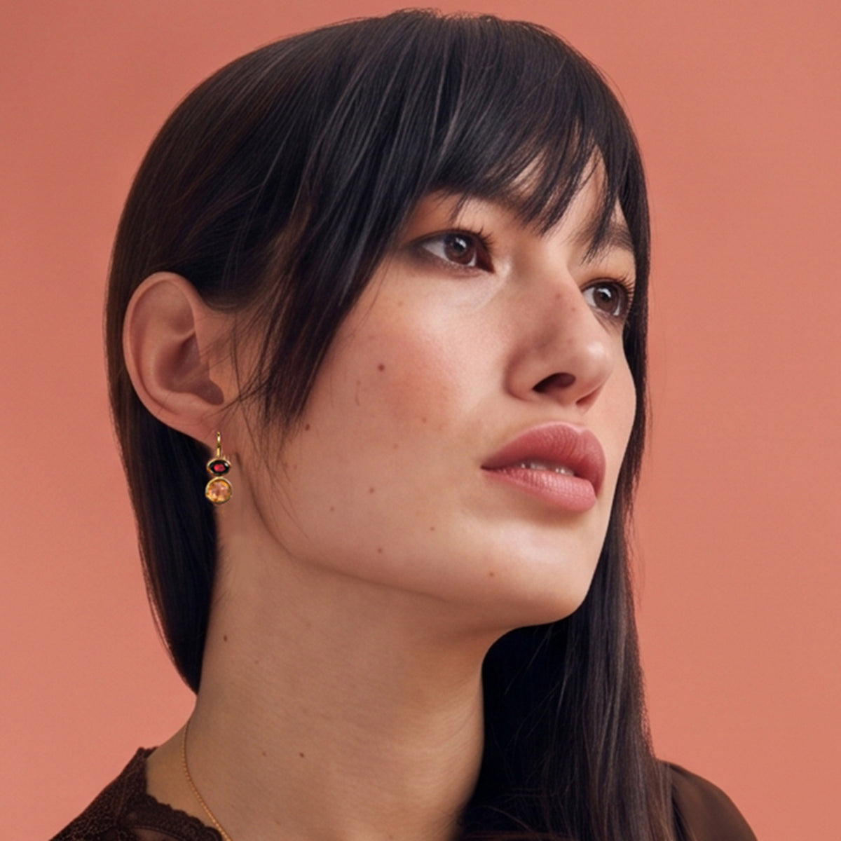 Woman wearing gold drop earrings in citrine and garnet alongside a close up of the matching necklace on a warm autumn terracotta colour