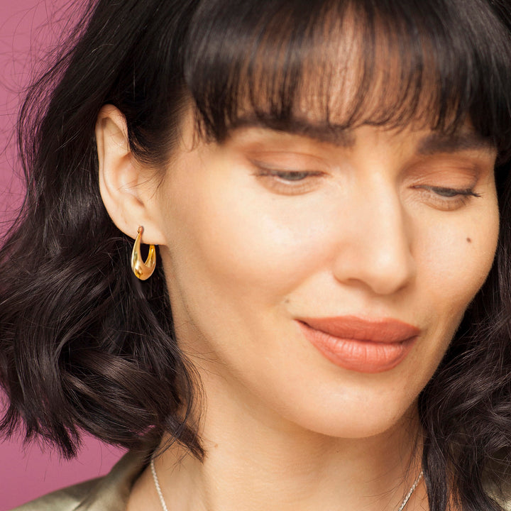 Close-up of a woman wearing gold hoop earrings with a pink background