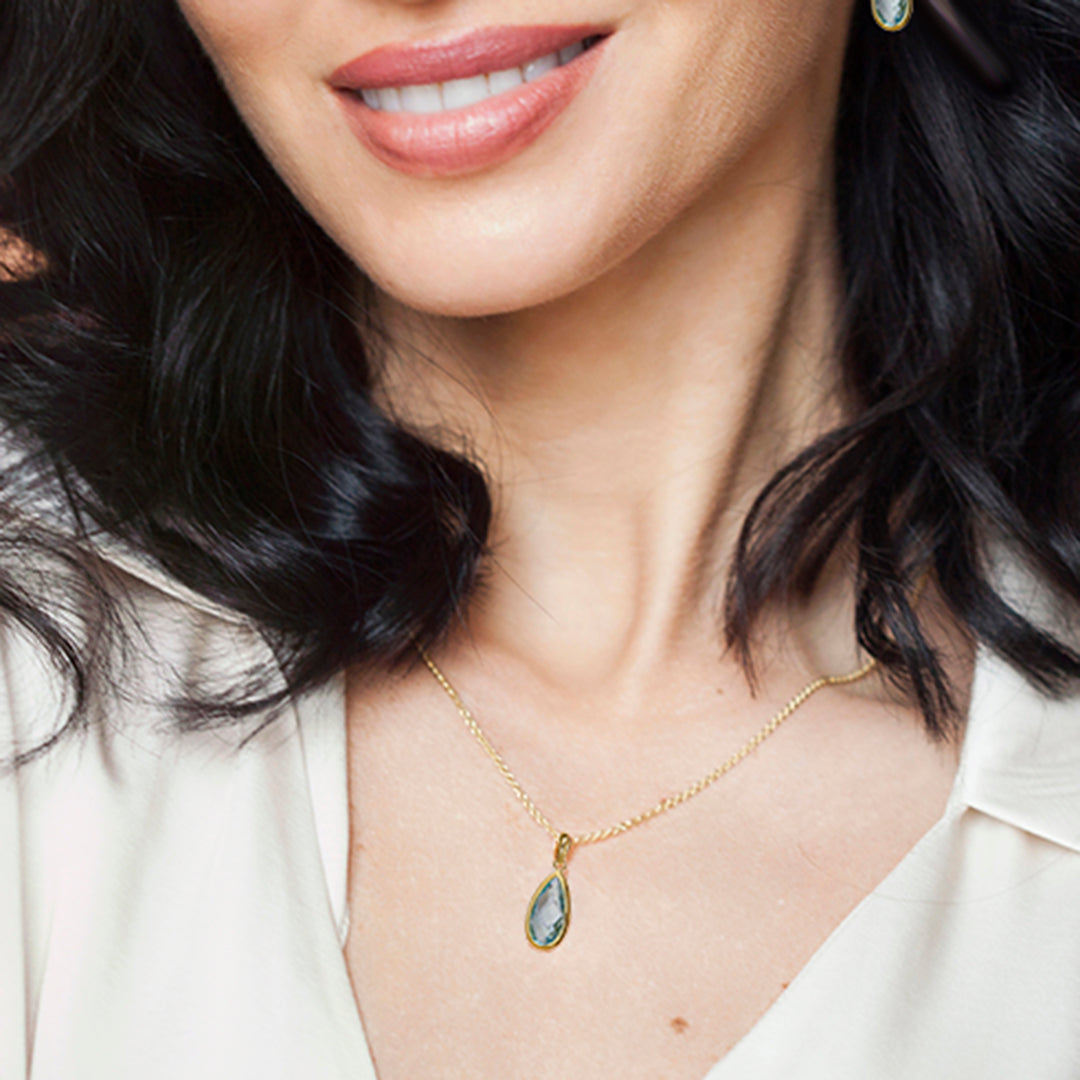Model wearing gold pear drop pendant necklace with blue topaz