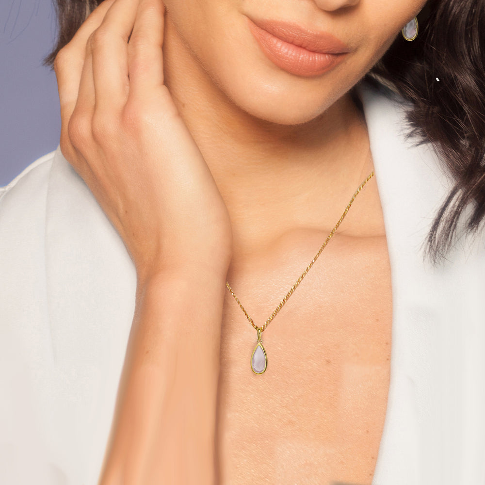 Close-up of woman wearing a teardrop shaped gold necklace with a pale pink gemstone