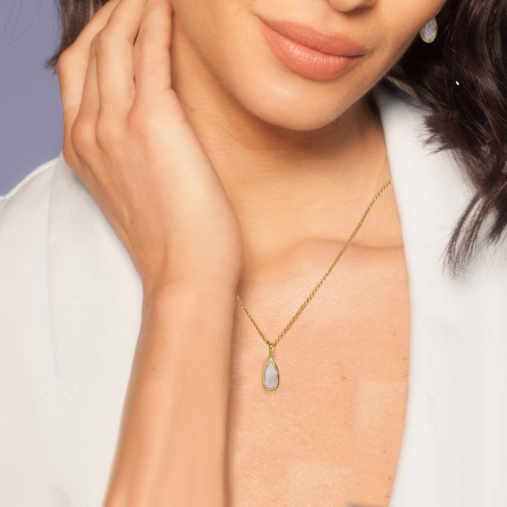 Close-up of woman wearing a teardrop shaped gold necklace with a pale pink gemstone