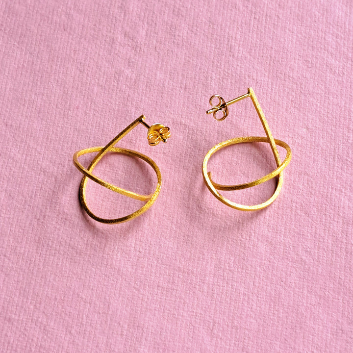 Gold vermeil spiral stud earrings on a pink background