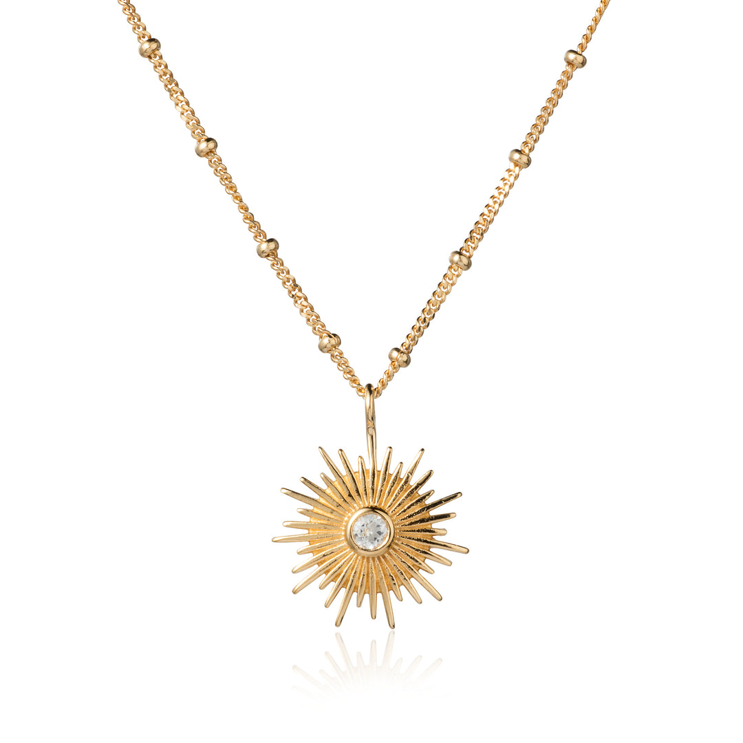 Gold sun necklace on a beaded curb chain featuring a white topaz gemstone pendant.