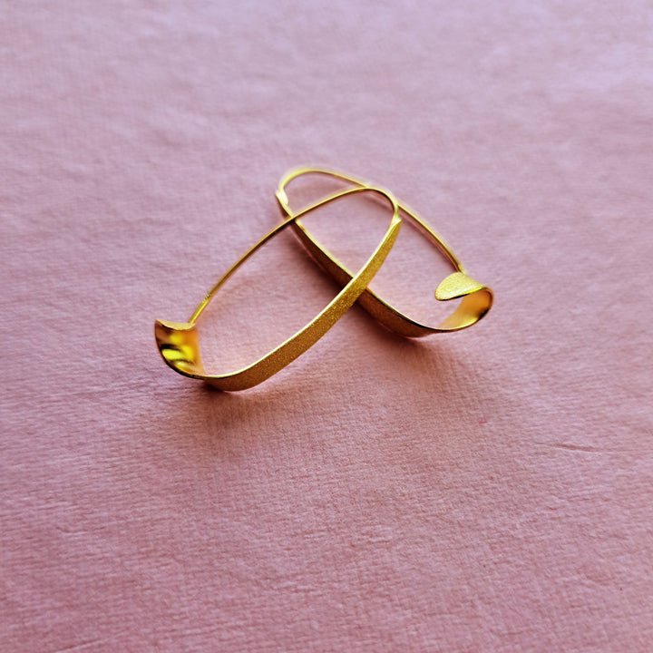 Alternative view of gold vermeil swirl threader hoop earrings on a pink background