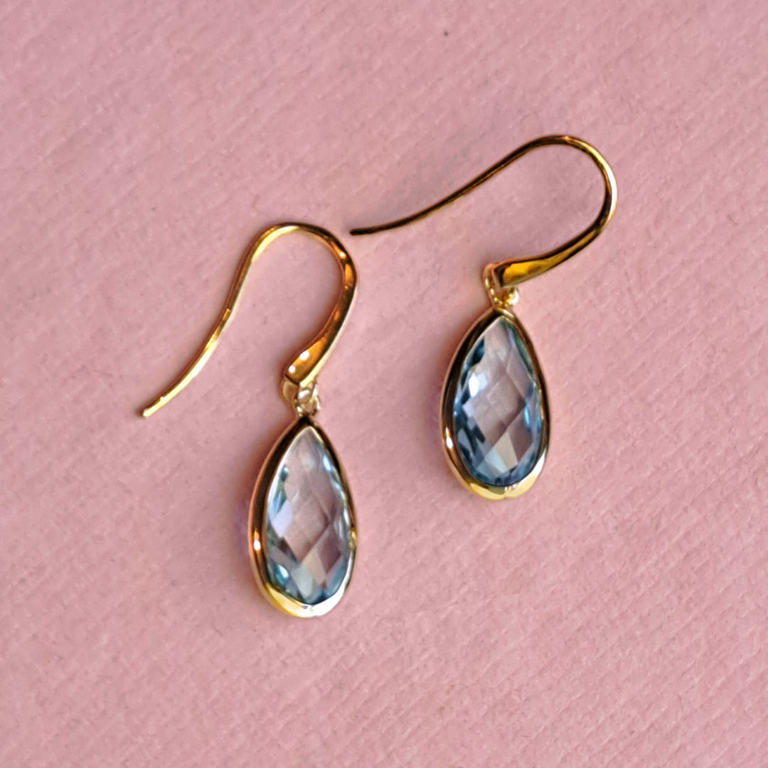 18ct gold vermeil pear drop earrings with blue topaz on a pink background