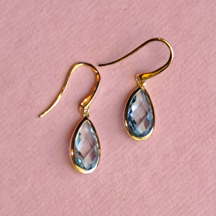 18ct gold vermeil pear drop earrings with blue topaz on a pink background
