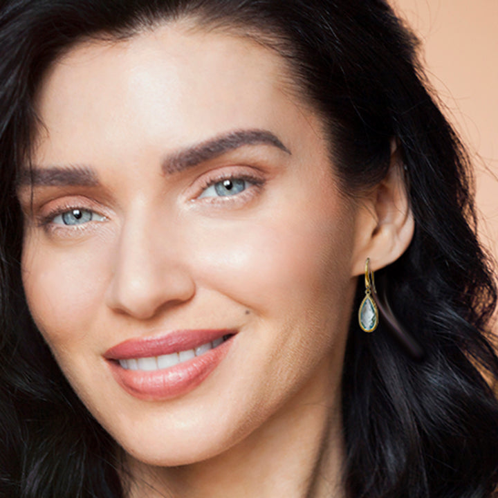 Close-up of model wearing gold teardrop earrings with blue topaz gemstones