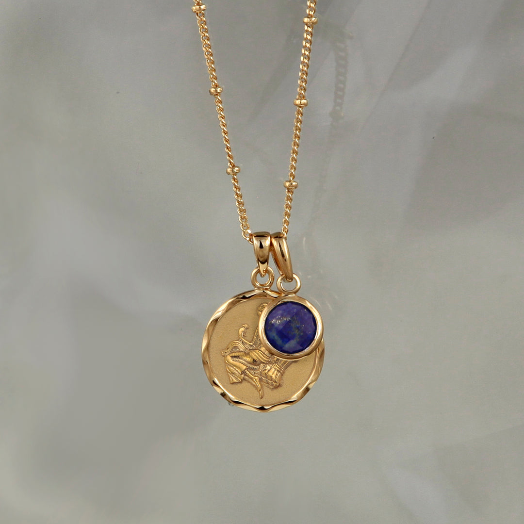 Gold Virgo star sign pendant with a lapis lazuli September birthstone charm on a gray background