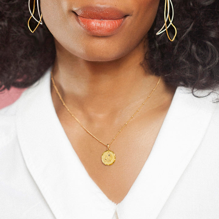 Model wearing a gold Virgo zodiac necklace and white blouse