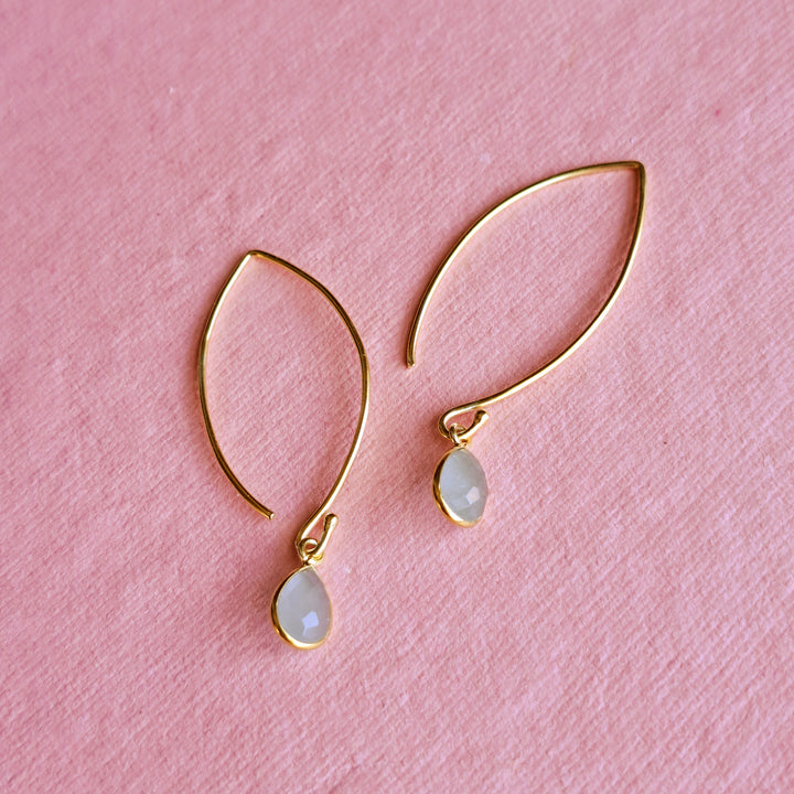 A pair of gold vermeil hook earrings with faceted aquamarine teardrop gemstones on a pink background.