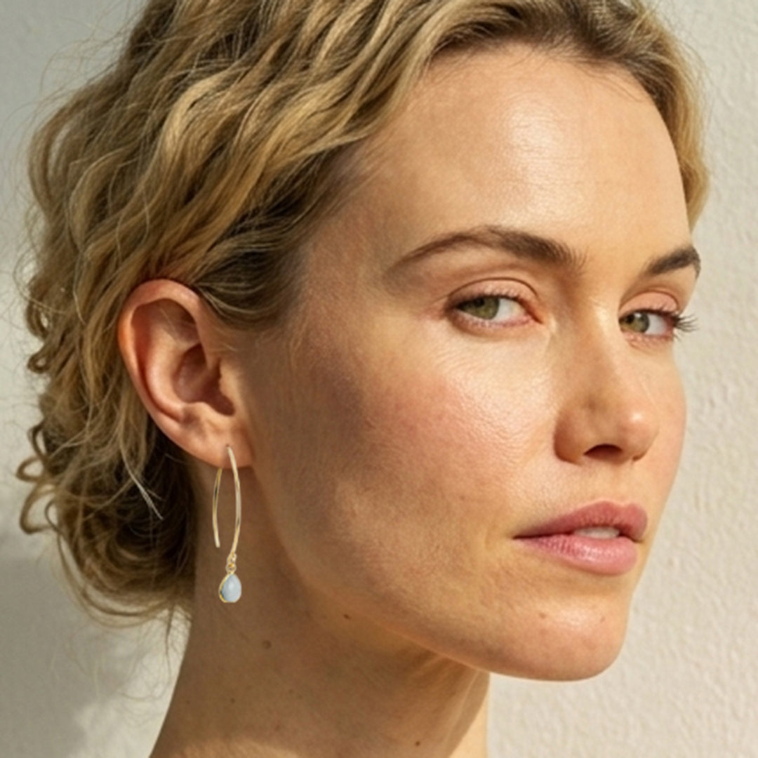 Model wearing gold threader style earrings with aquamarine tearshaped drops.