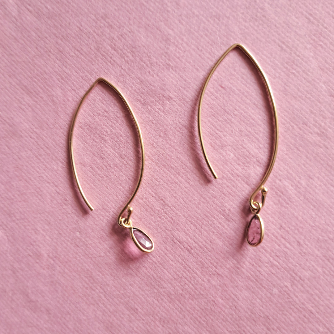 Modern gold vermeil threader earrings with natural tourmaline pear-cut gemstone drops on a pink background.