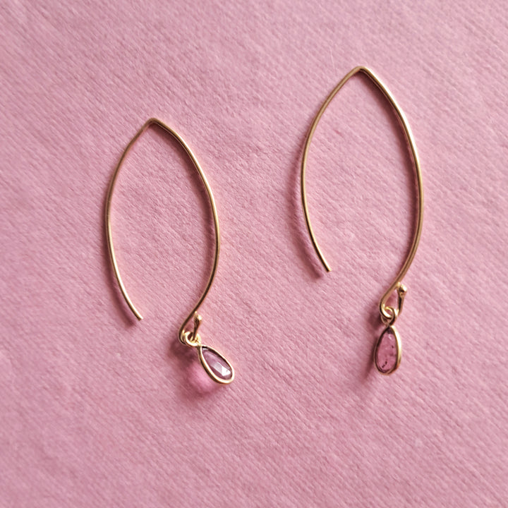 Modern gold vermeil threader earrings with natural tourmaline pear-cut gemstone drops on a pink background.