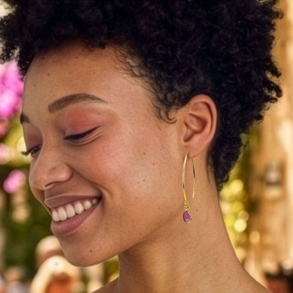 Smiling woman  wearing gold threader style earrings with pink tourmaline drops.