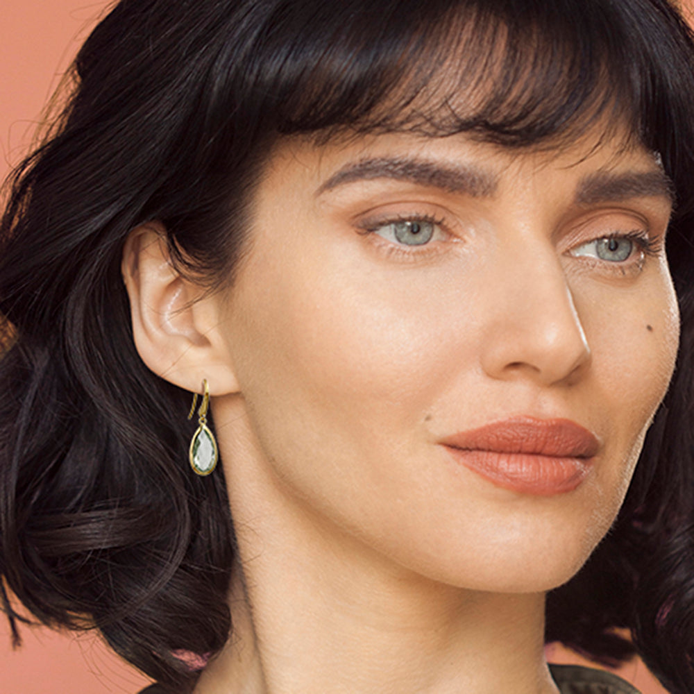 Close-up of a woman's face with dark hair and wearing gold teardrop earrings with pale green amethyst gemstones