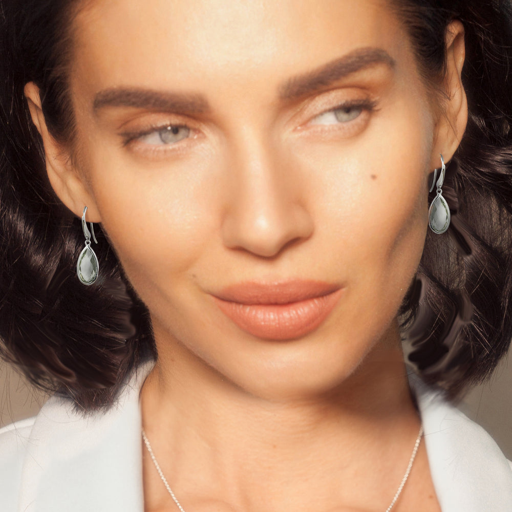 Close-up of a woman wearing silver teardrop shaped earrings with pale green amethyst gemstones.