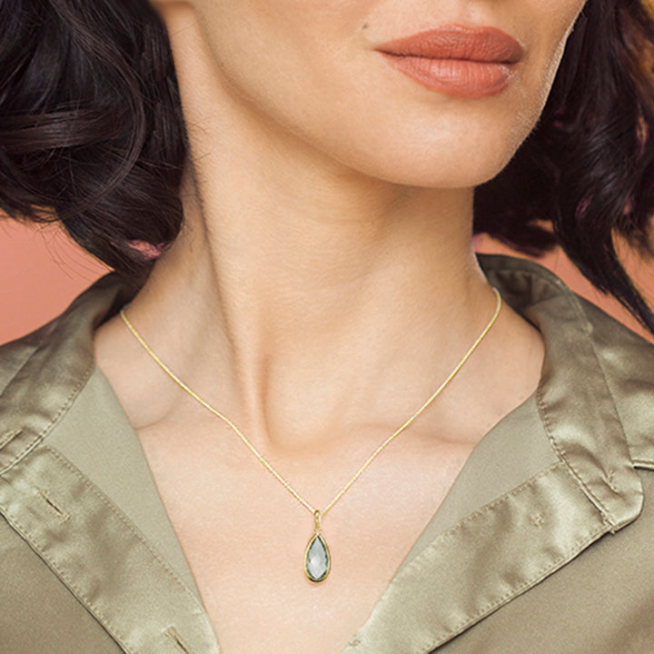 Woman wearing a gold necklace with a teardrop green amethyst pendant