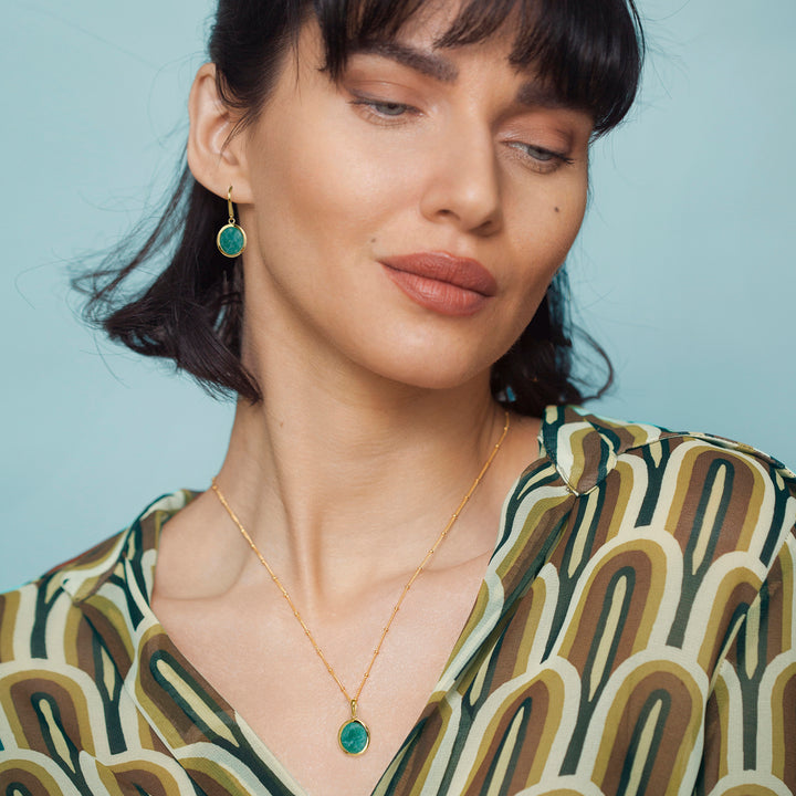 Woman wearing a gold amazonite necklace with green earrings against a light blue background