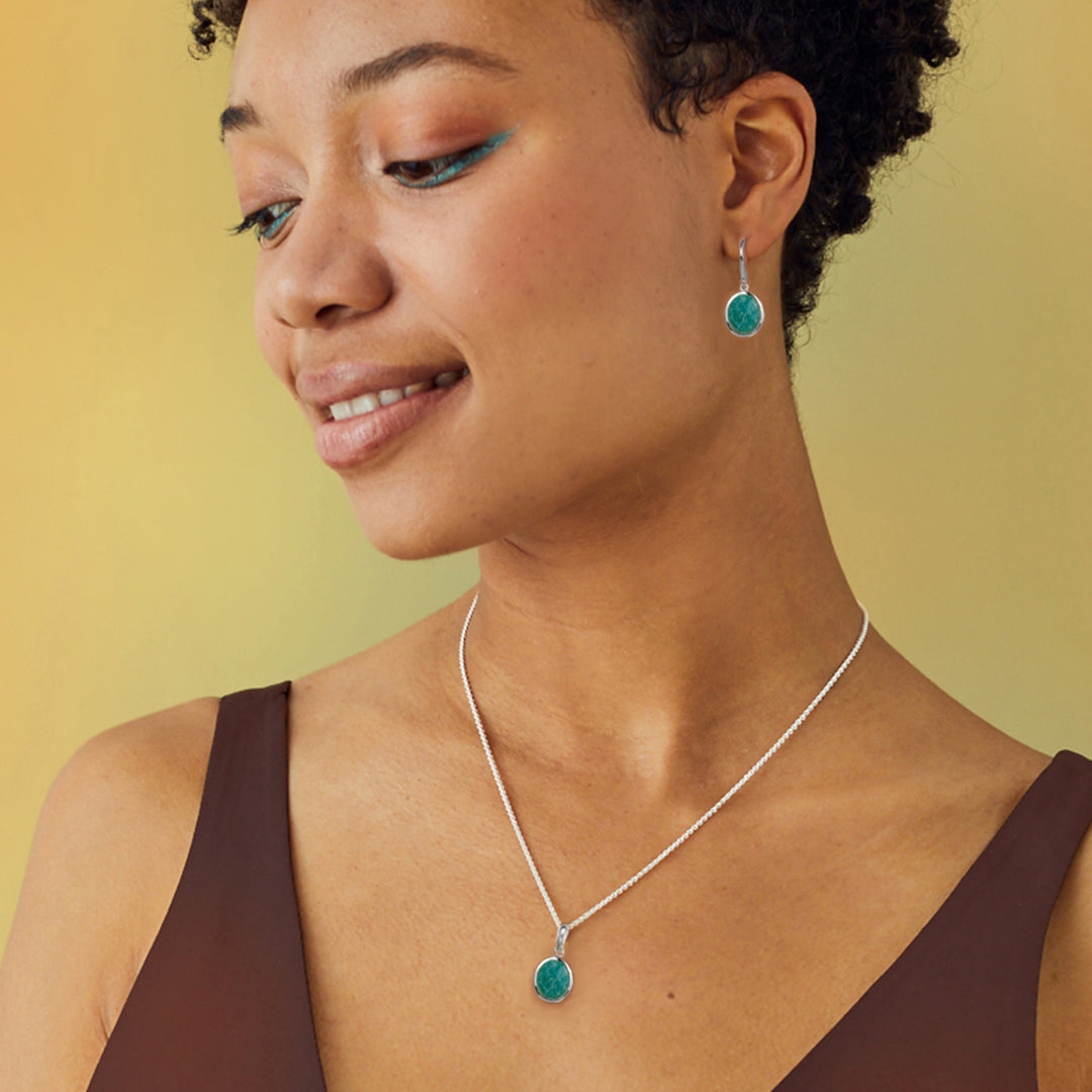 Woman wearing a silver amazonite necklace and turquoise earrings against a yellow background