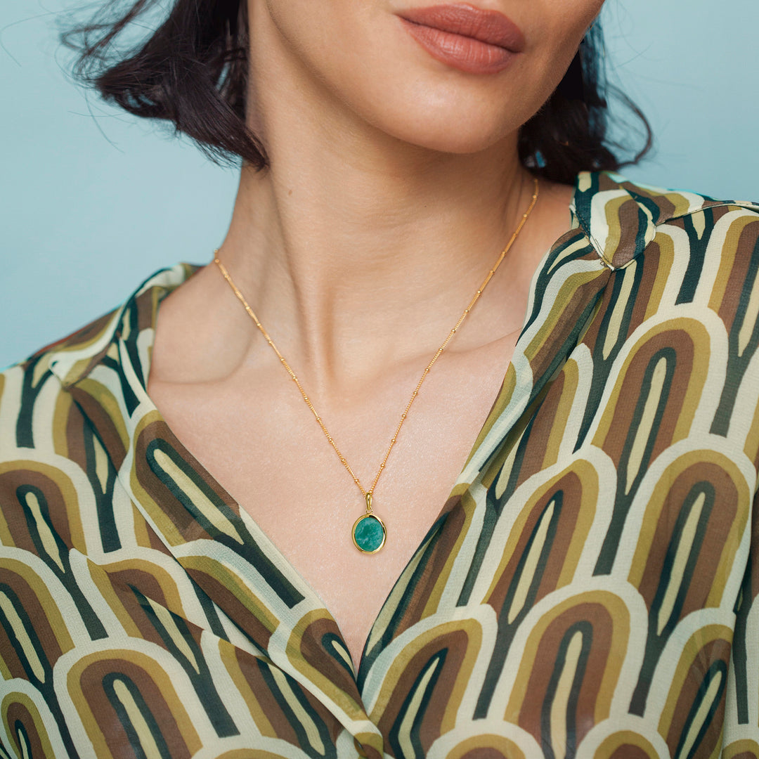 Woman wearing a gold amazonite necklace with a blue gemstone against a light blue background