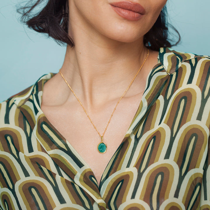 Woman wearing a gold amazonite necklace with a blue gemstone against a light blue background
