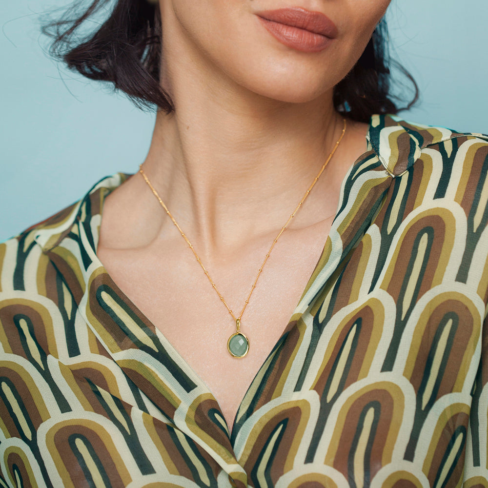 Close-up of a model wearing a gold aventurine necklace with a green gemstone, against a neutral background.