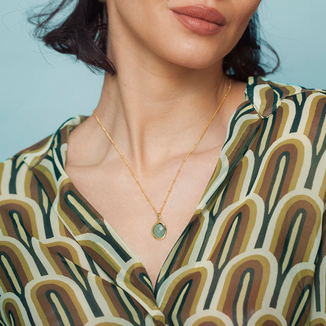 Close-up of a model wearing a gold aventurine necklace with a green gemstone, against a neutral background.