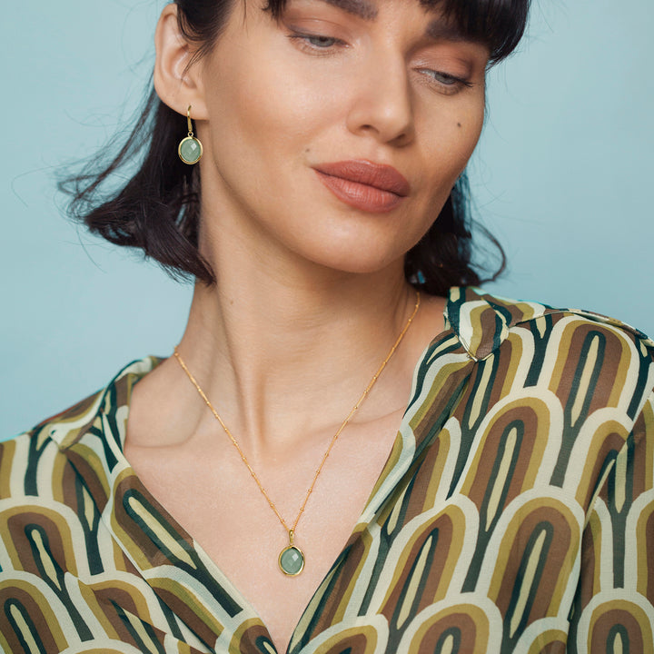 Woman wearing a silver aventurine necklace and green gemstone earrings with a light blue background