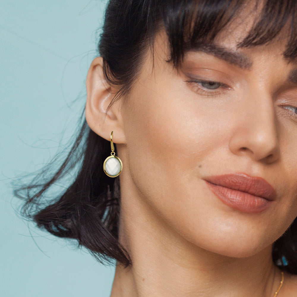 Close-up of a woman wearing gold moonstone earrings with a light blue background