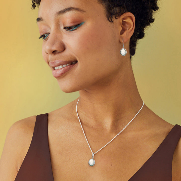 Woman wearing a silver moonstone necklace and earrings against a yellow background