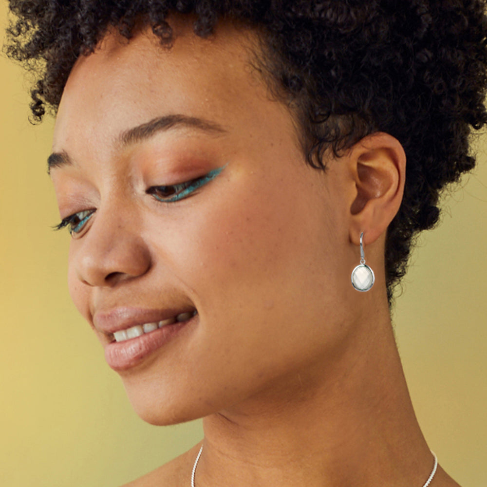 Close-up of a woman wearing silver moonstone drop earrings with a yellow background