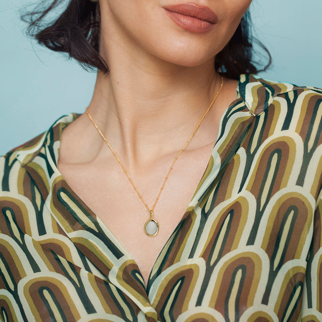 Woman wearing a gold moonstone necklace with a white gemstone close-up of neck and patterned top.