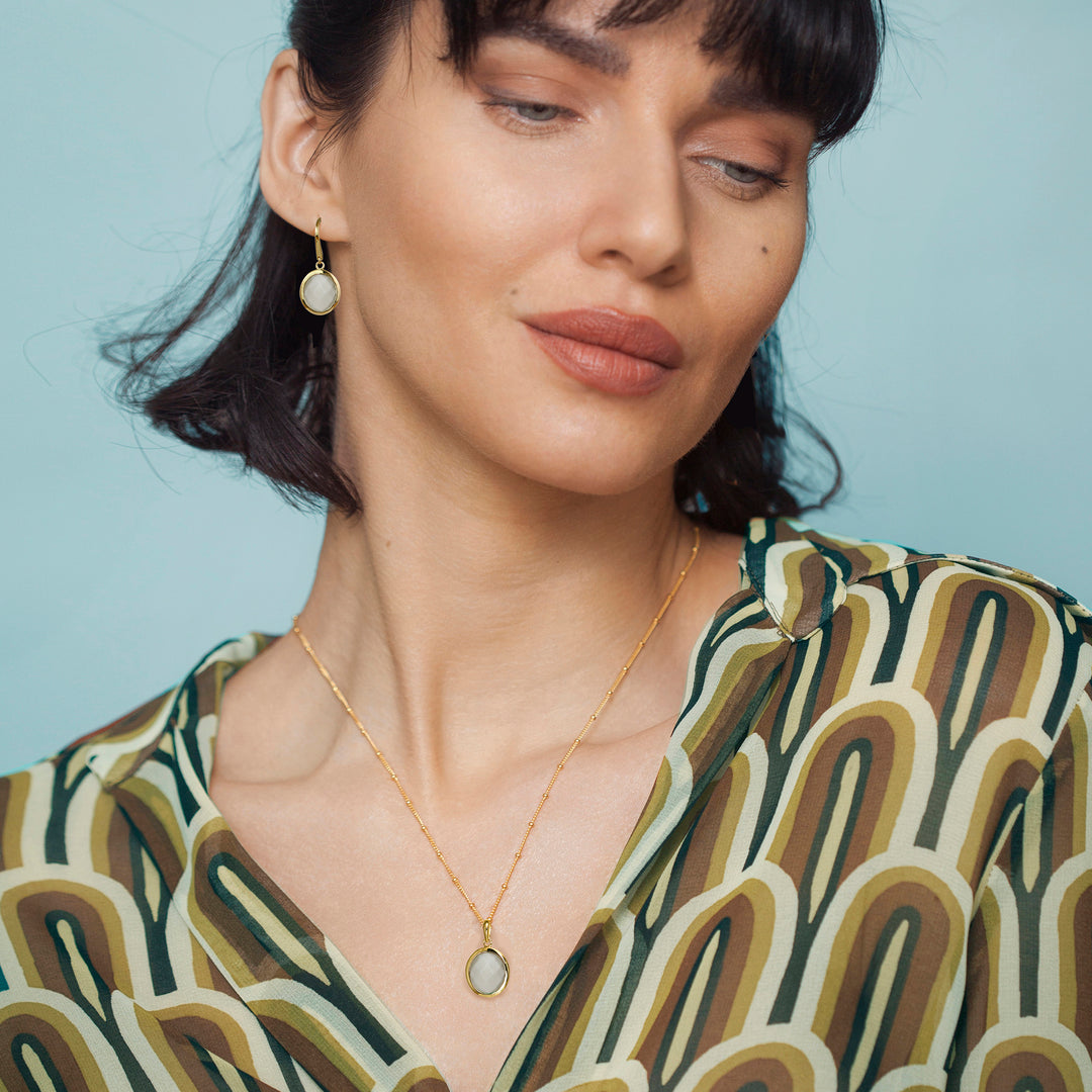 Woman wearing a gold moonstone necklace and earrings with a light blue background