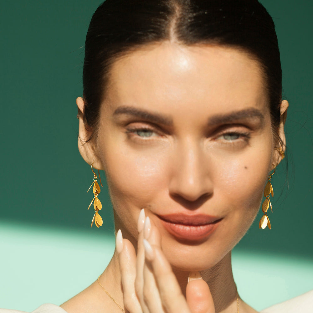 Model wearing gold vermeil long drop catkin flower earrings with a floral design with green background