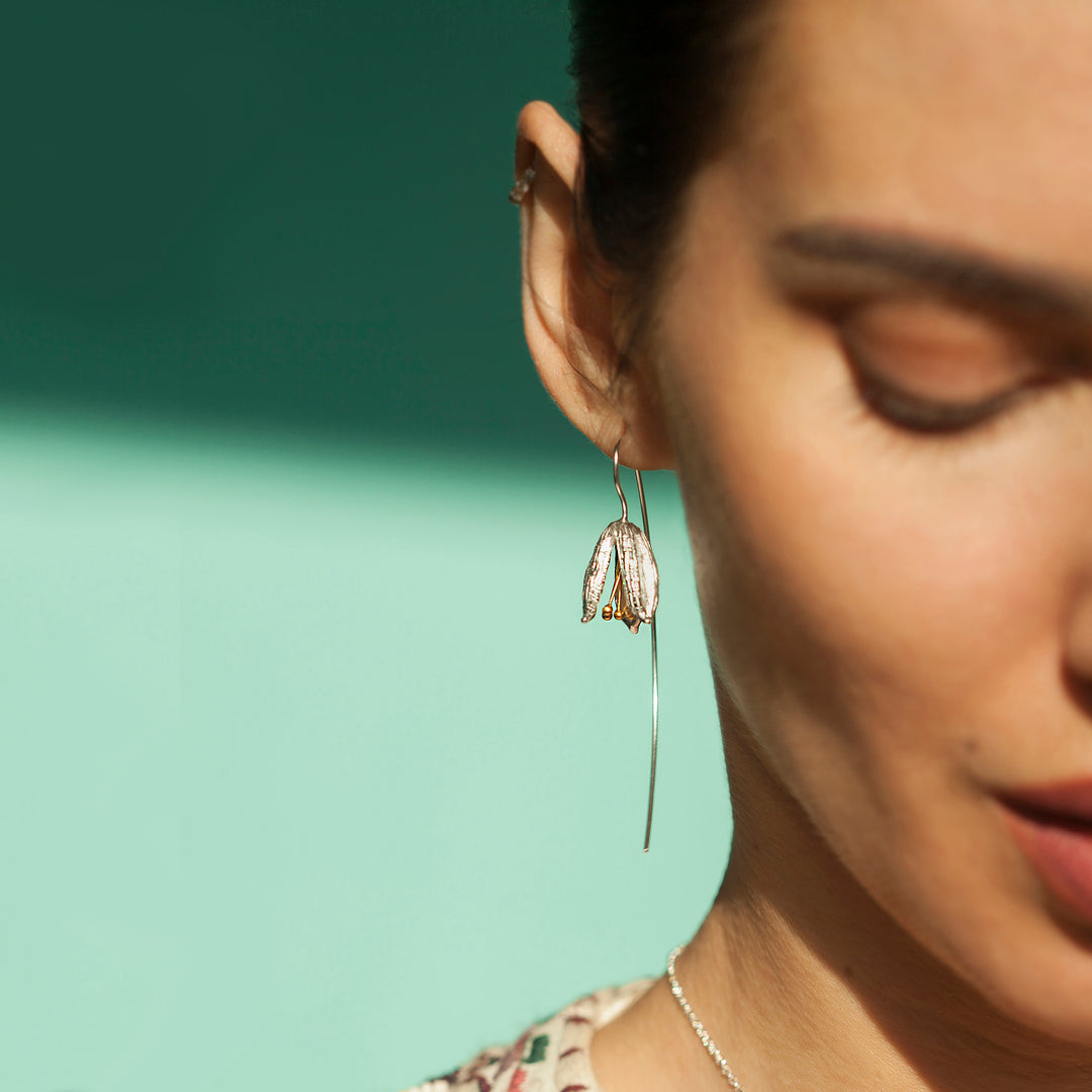Close-up of a woman wearing a delicate silver earring with a green background