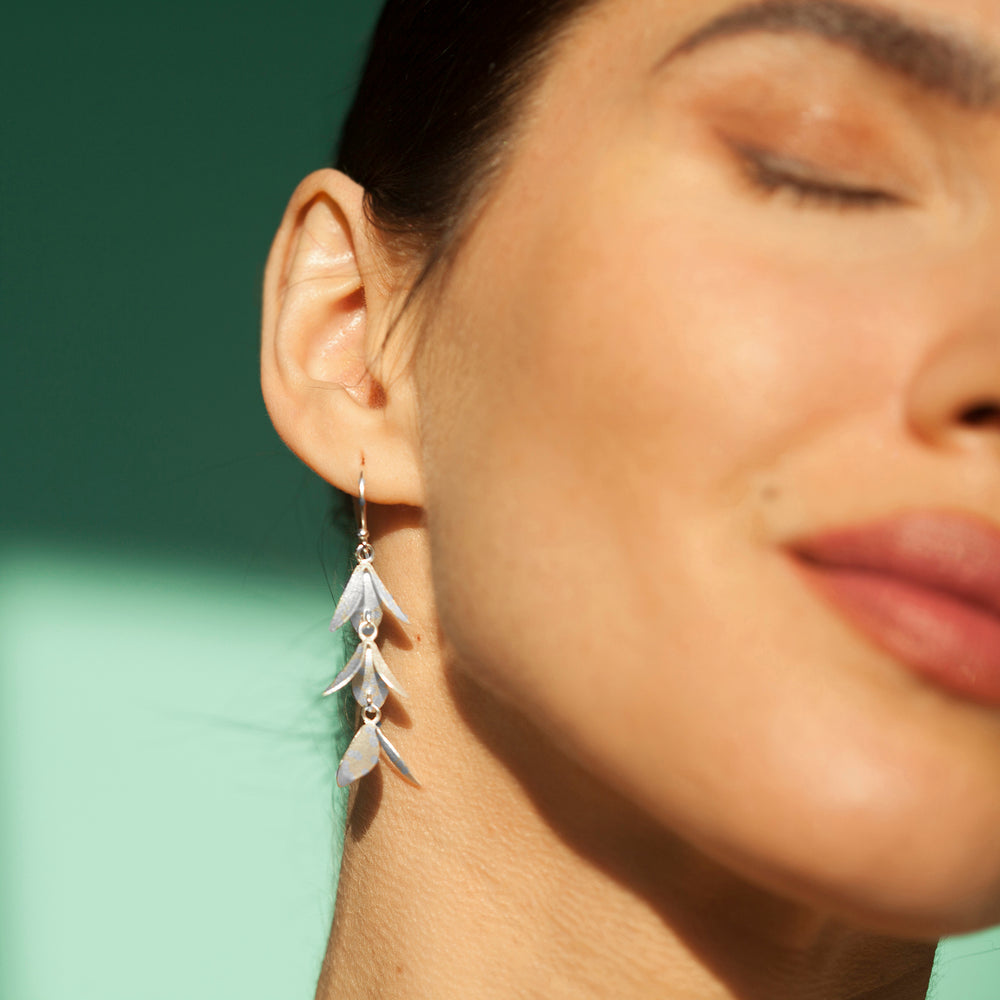 Close-up of a woman wearing a silver catkin-shaped earring against a green background