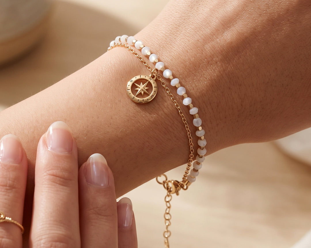 White moonstone beaded bracelet with compass charm on a woman's wrist