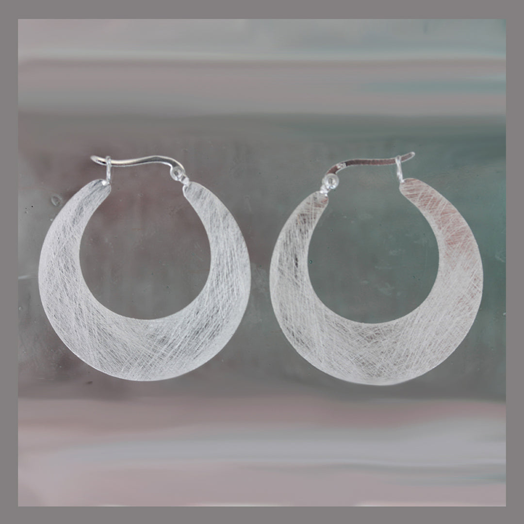 Silver hoop snap-post earrings on a reflective gray surface 