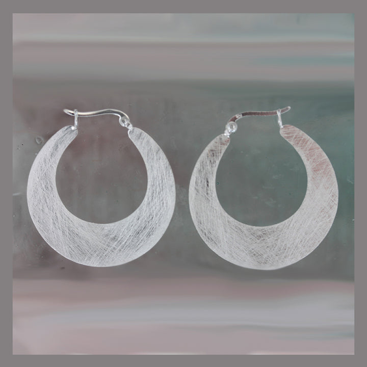 Silver hoop snap-post earrings on a reflective gray surface 