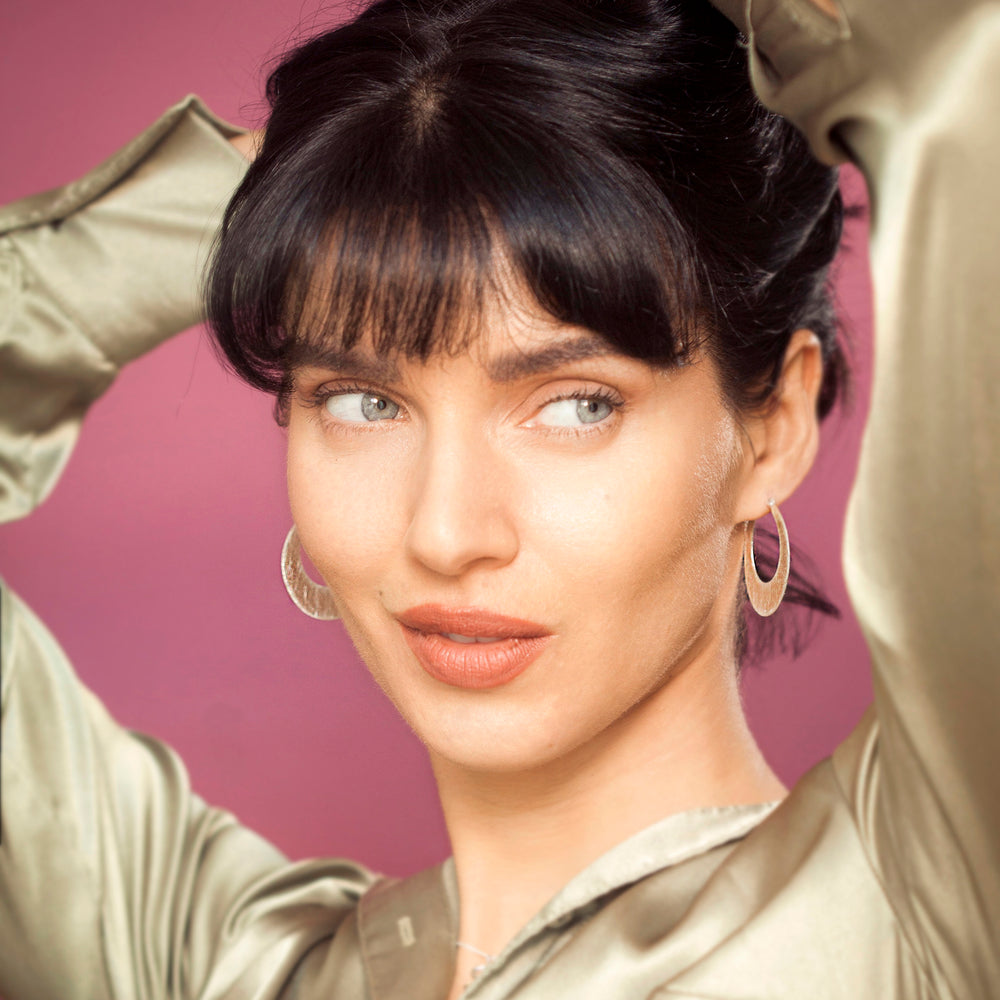 Woman wearing silver hoop earrings against a pink background