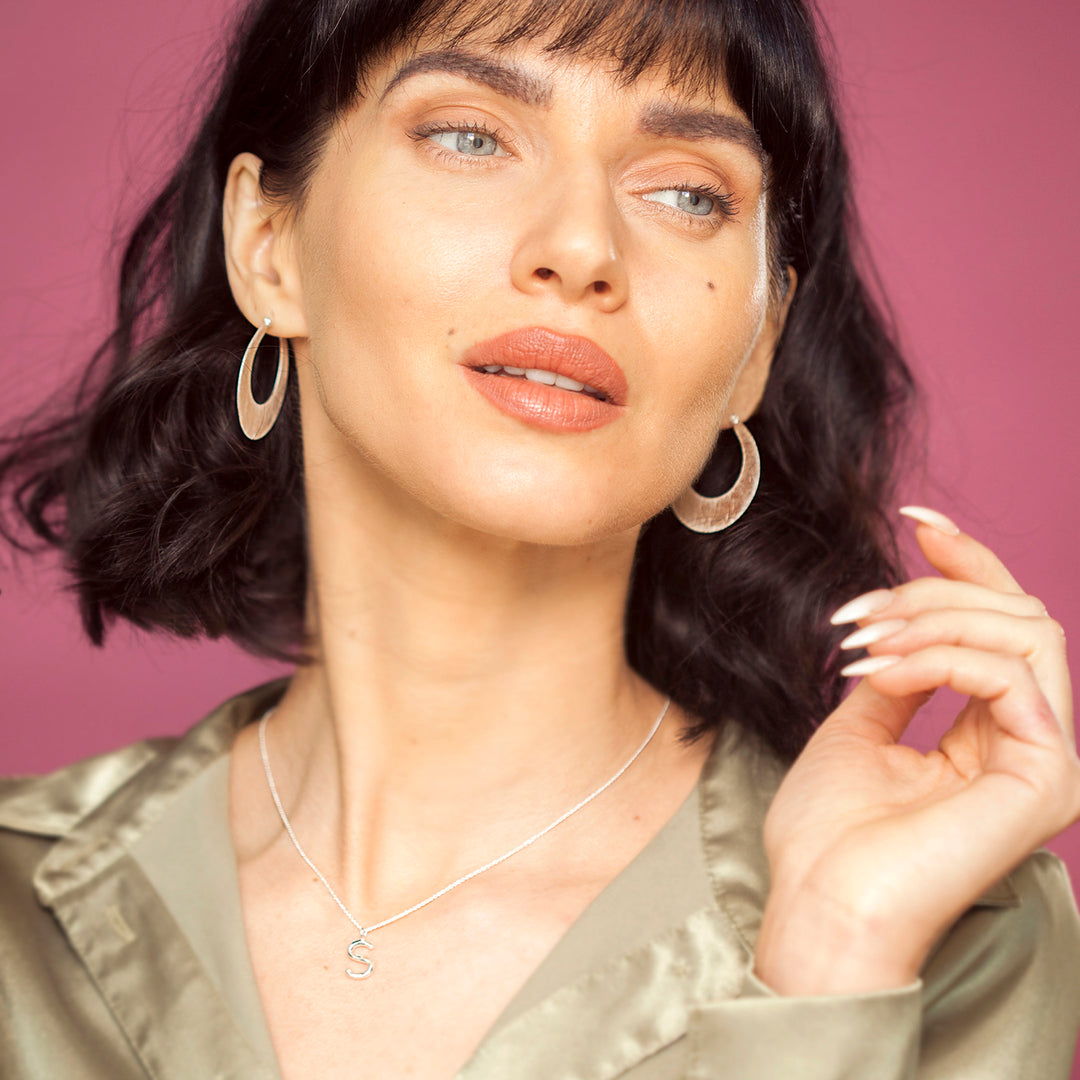 Woman wearing silver hoop earrings and a silver necklace against a pink background