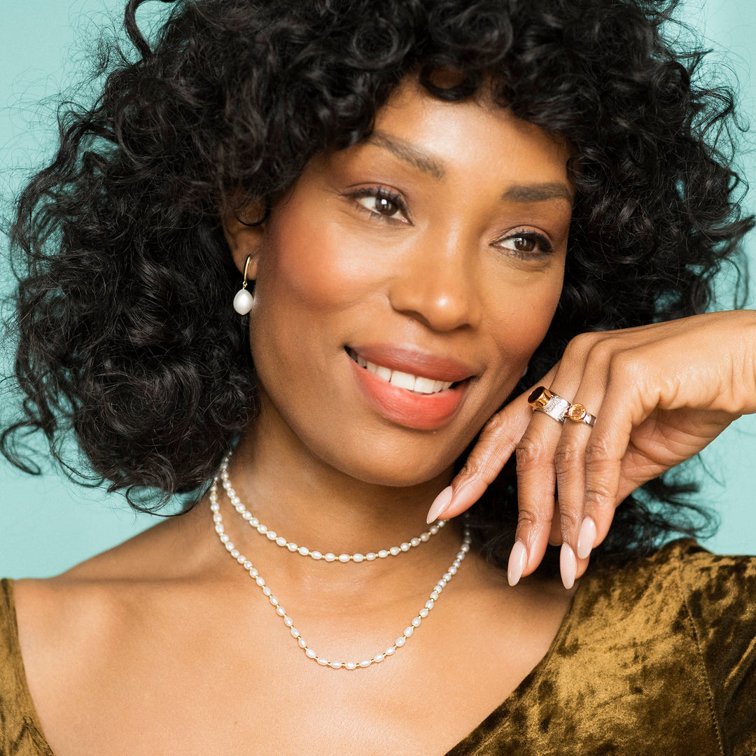 Woman wearing two gold and freshwater pearl necklaces with earrings and rings.