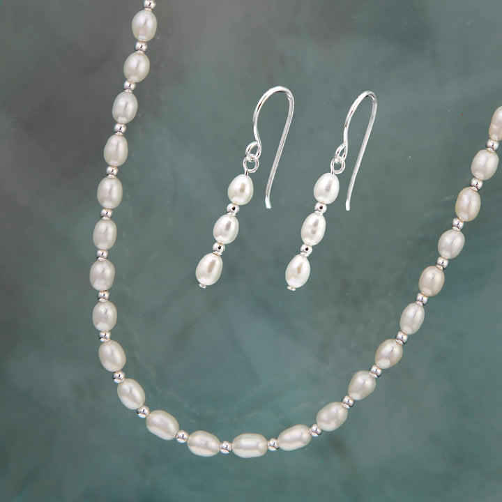 Silver and seed pearl necklace and earrings set on a textured gray background