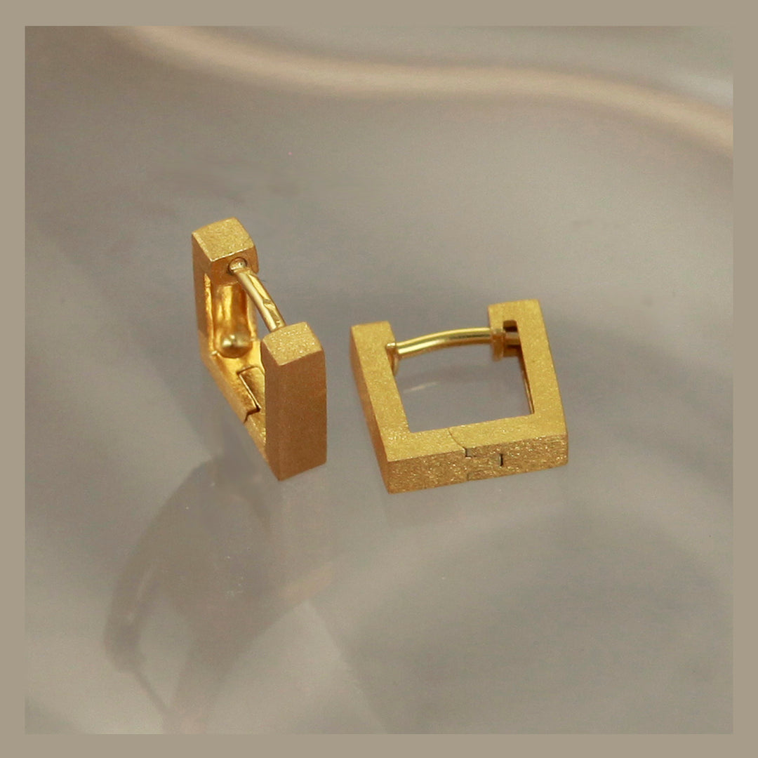 Gold square hoop earrings on a reflective surface