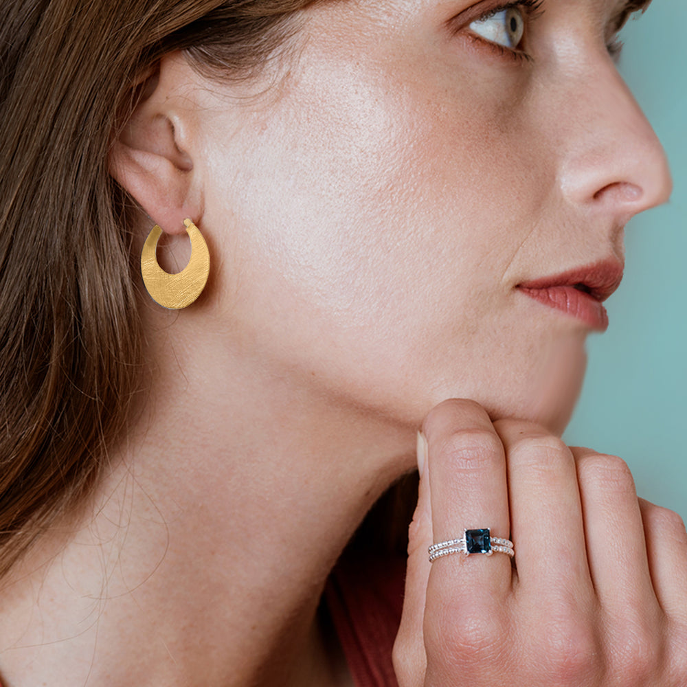 Close-up of a woman wearing gold hoop earrings and a ring with a blue gemstone.